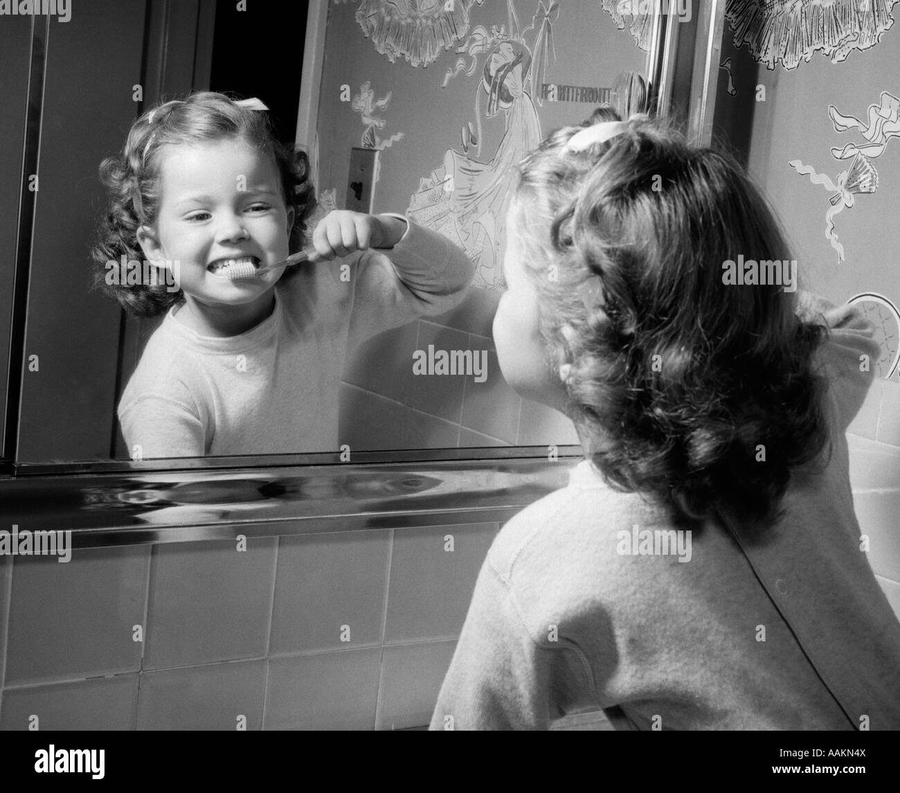 Anni Cinquanta ragazza guardando nello specchio del bagno la spazzolatura dei denti Foto Stock