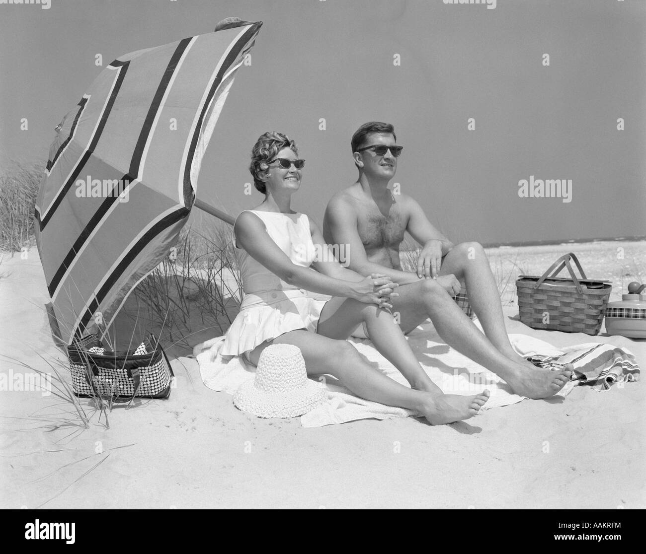 Anni sessanta paio di occhiali da sole seduto sulla spiaggia coperta con le gambe estese con ombrellone Foto Stock