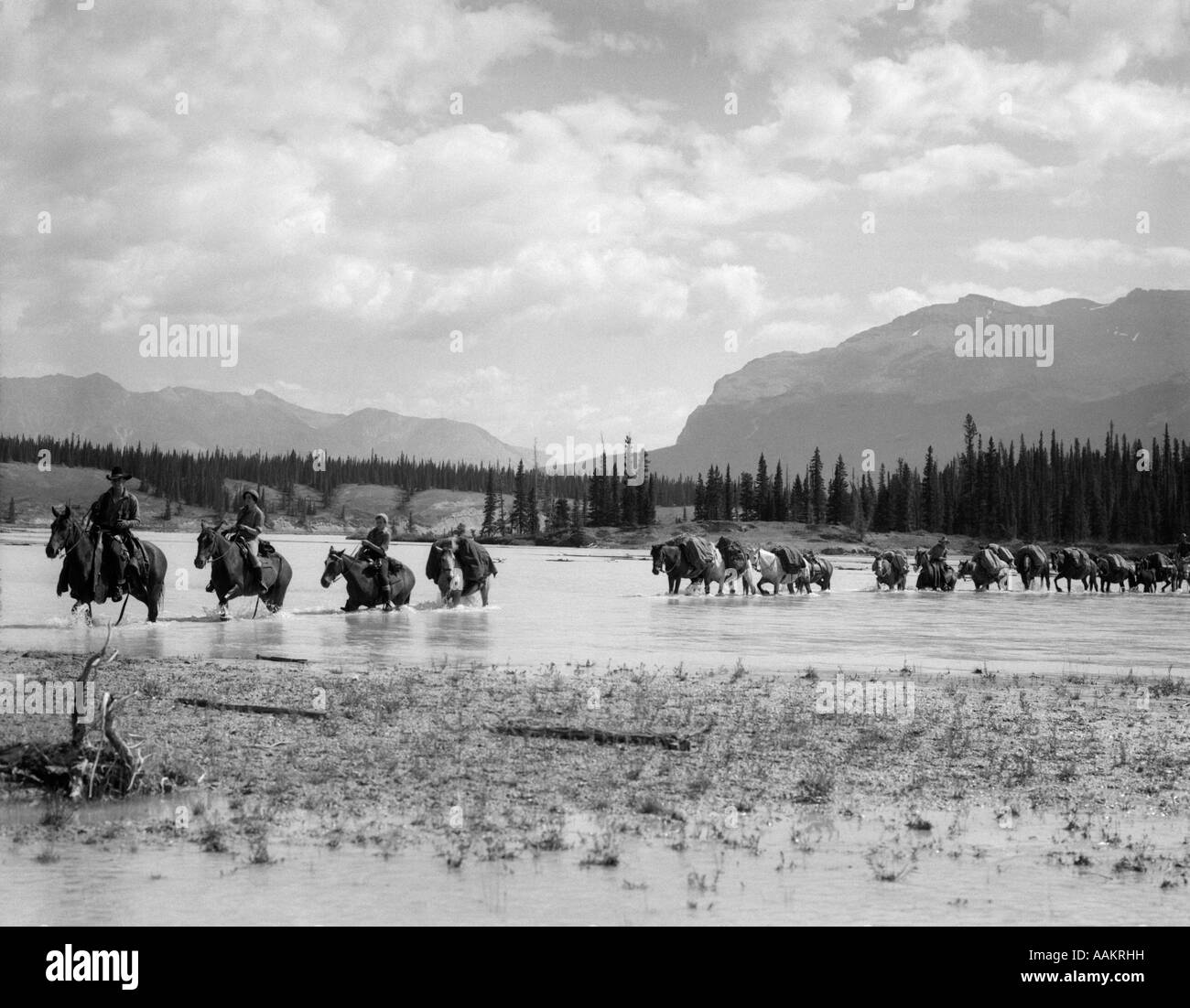 1930 Gruppo quattro uomini a cavallo attraverso la parte poco profonda del fiume LINEA DI CAVALLI DIETRO IL FIUME DI CAVALLO ALTA Foto Stock