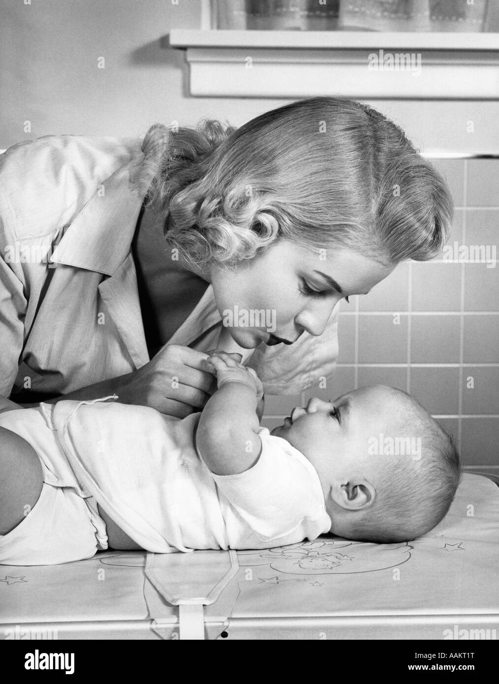 Anni Cinquanta madre donna PIEGAMENTI Bambino giacente sul corredino tenendo le mani a parlare Foto Stock