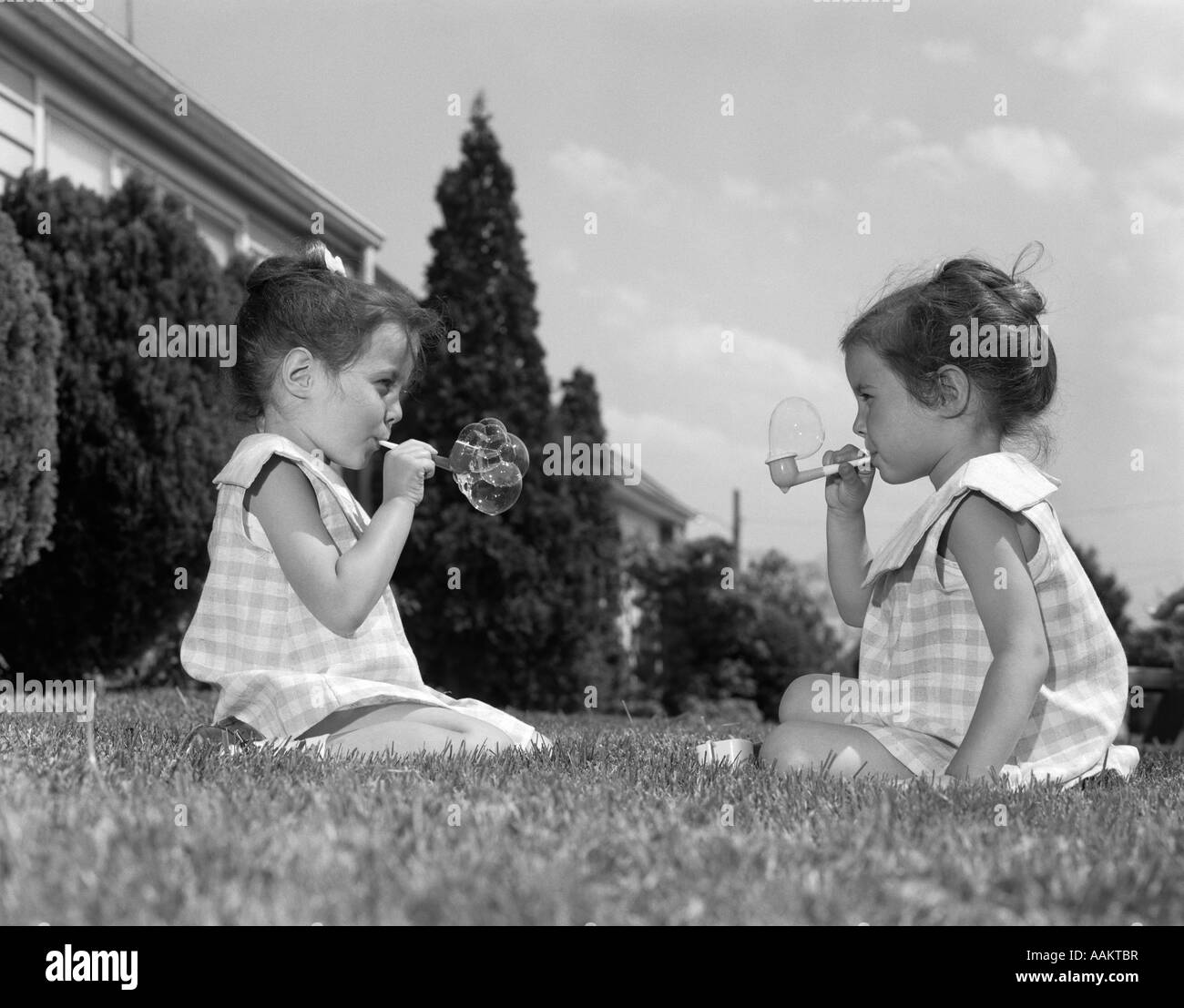 Anni sessanta figlie gemelle seduta erba soffiare bolle OUTDOOR Divertimento estivo Foto Stock