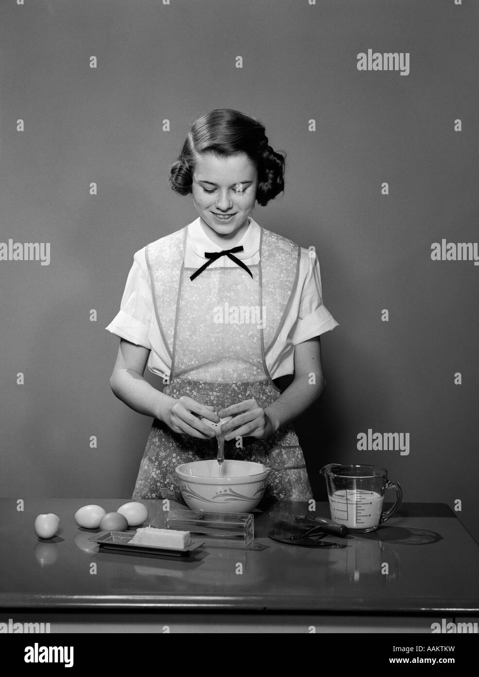 Anni Cinquanta giovane ragazza adolescente che indossa il grembiule uovo di frenatura nel recipiente di cottura di cottura Foto Stock