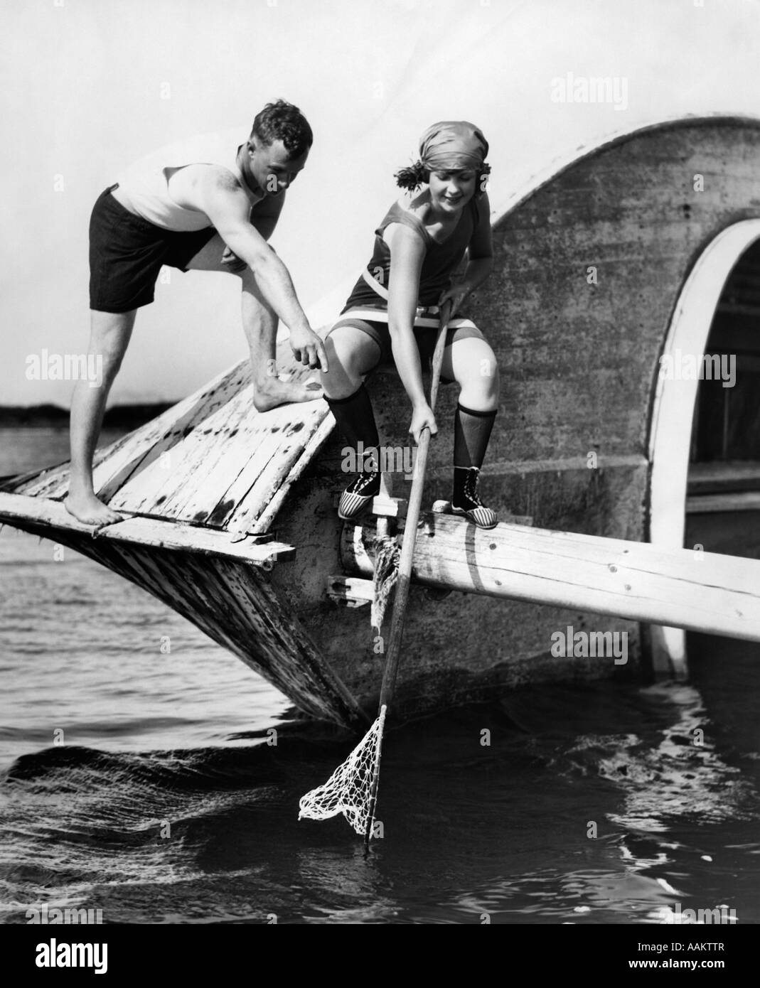 1920s L UOMO E LA DONNA IN COSTUME DA pescato granchi off vecchia abbandonato la barca di legno Foto Stock