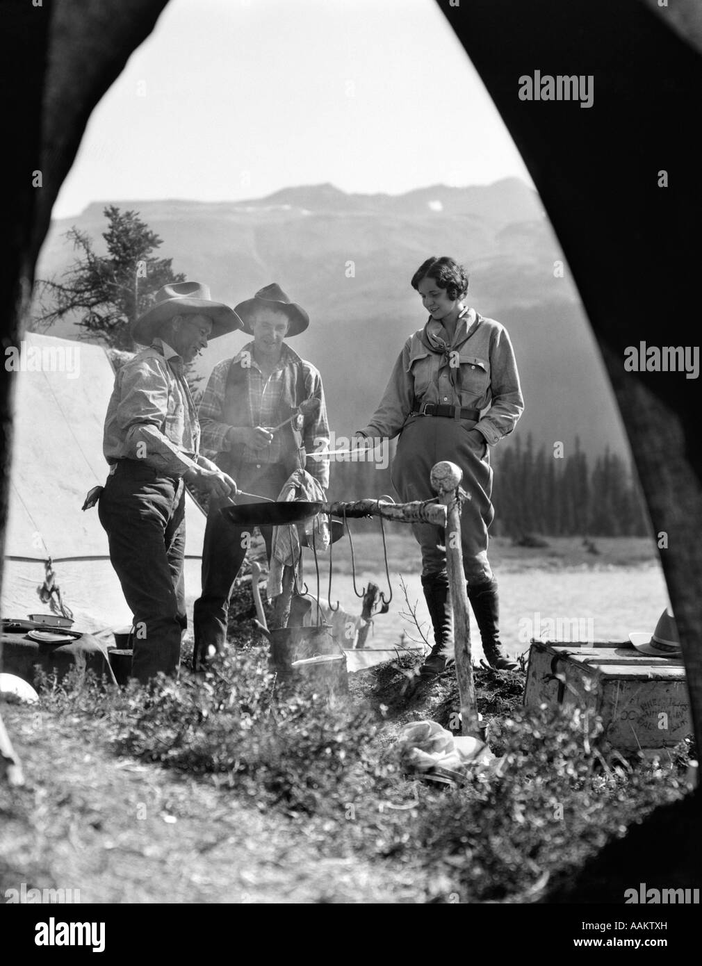 1930 Campeggio Al Lago Bow Alberta Canada 2 uomini 1 donna in piedi intorno al falò Foto Stock