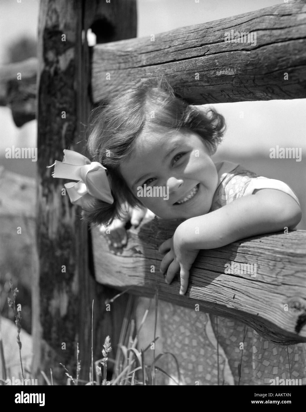 1930s sorridente bambina BOW nei capelli PEEKING TESTA tra rotaie di recinzione di legno Foto Stock