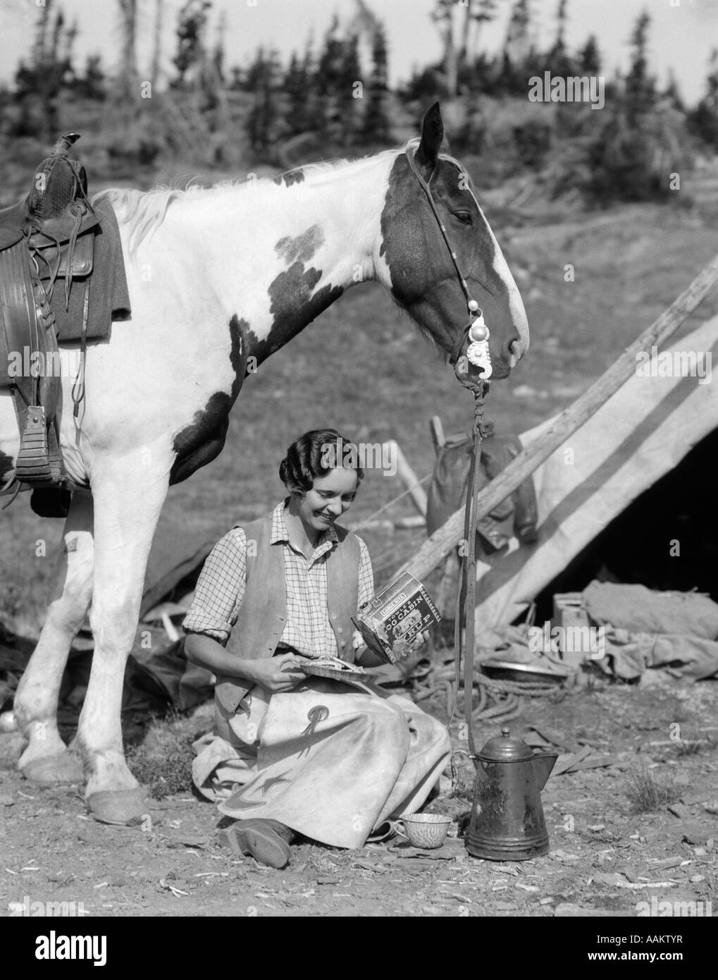 1920s 1930 donna seduta al di fuori della tenda accanto a PINTO cavallo di sciroppo di colata da stagno su frittelle GIUBBOTTO DA INDOSSARE E CHAPS Foto Stock