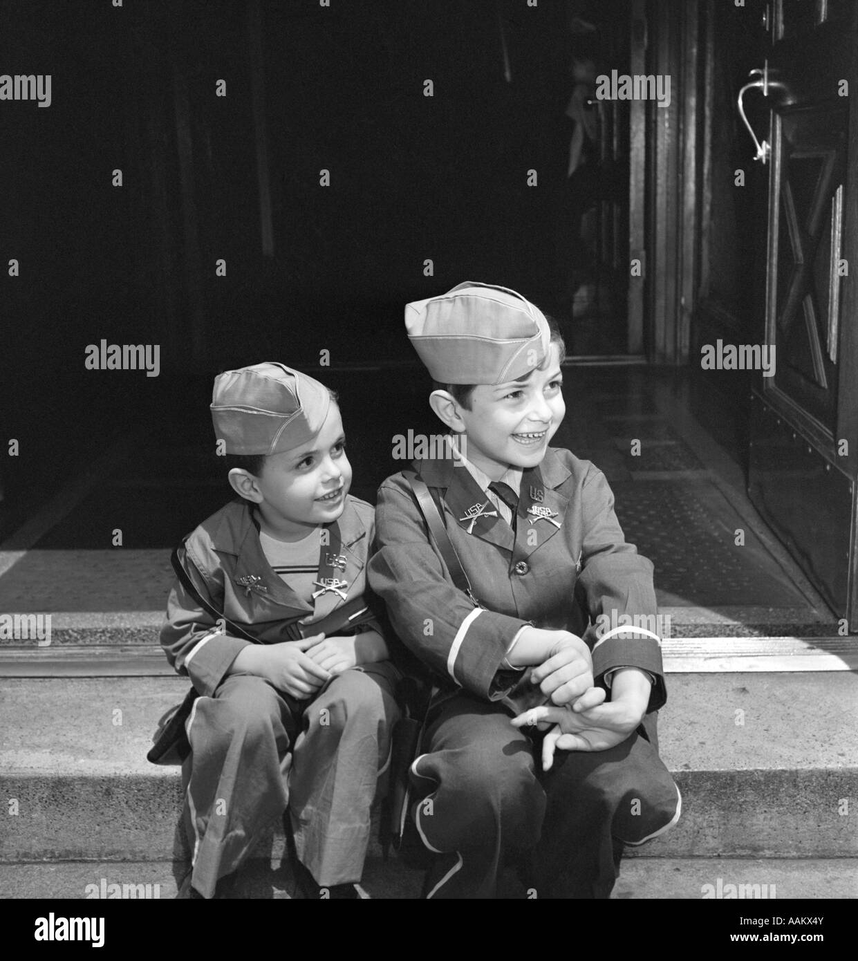 Negli anni quaranta due ragazzi sorridenti che indossano uniformi militari seduti sulla parte anteriore STOOP FIANCO A FIANCO Foto Stock