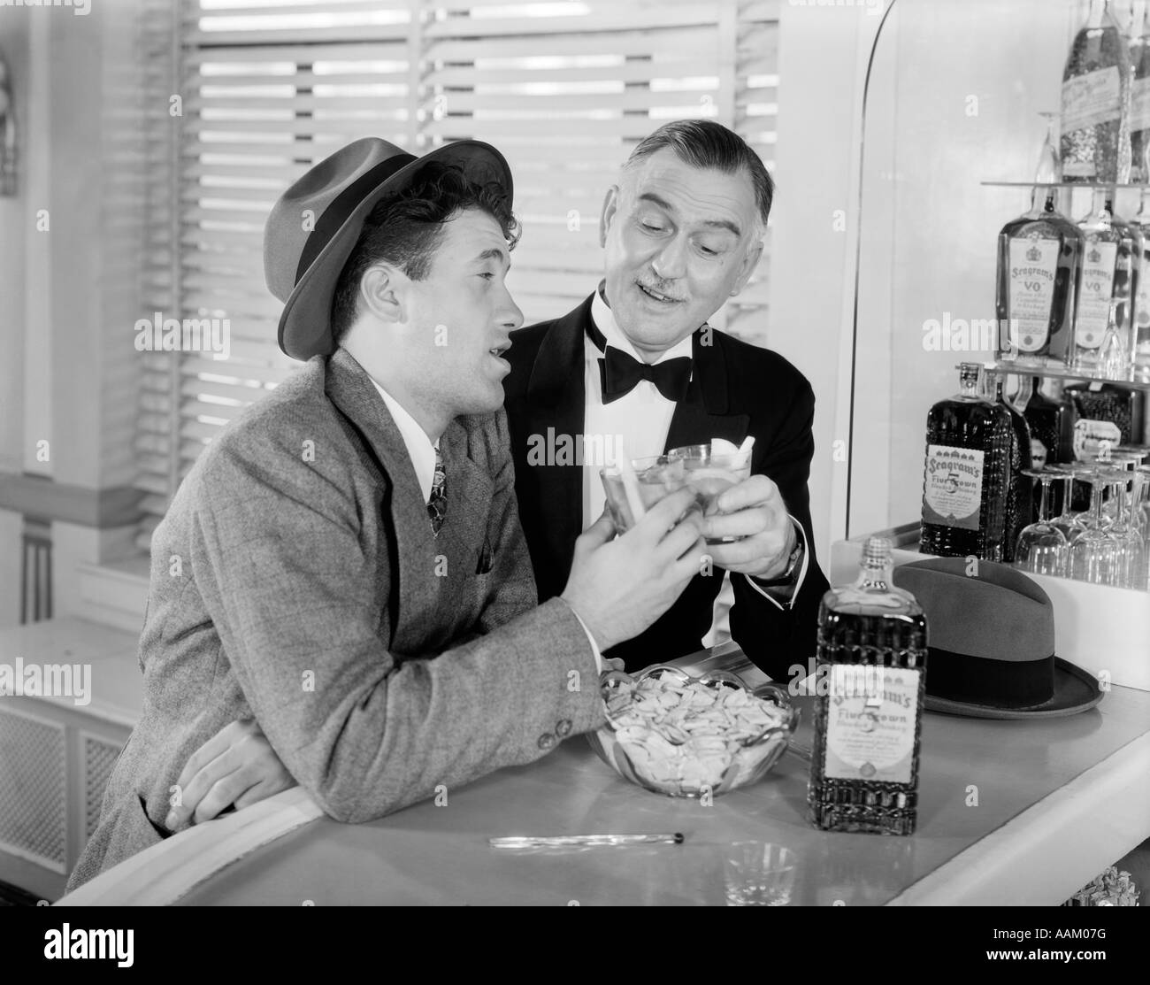 Negli anni quaranta anni cinquanta uomini al bar a bere whisky tostare un elegante ragazzo in smoking E UN IMPRENDITORE ubriachi Foto Stock