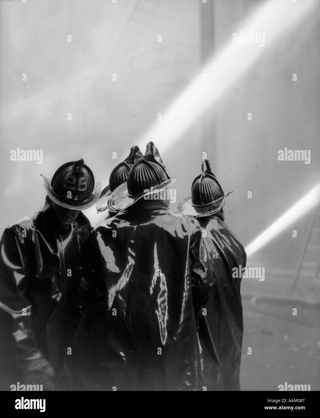 1920s vista posteriore di quattro VIGILI DEL FUOCO IN NERO SLICKERS SCHIZZARE I DUE TUBI FLESSIBILI Foto Stock