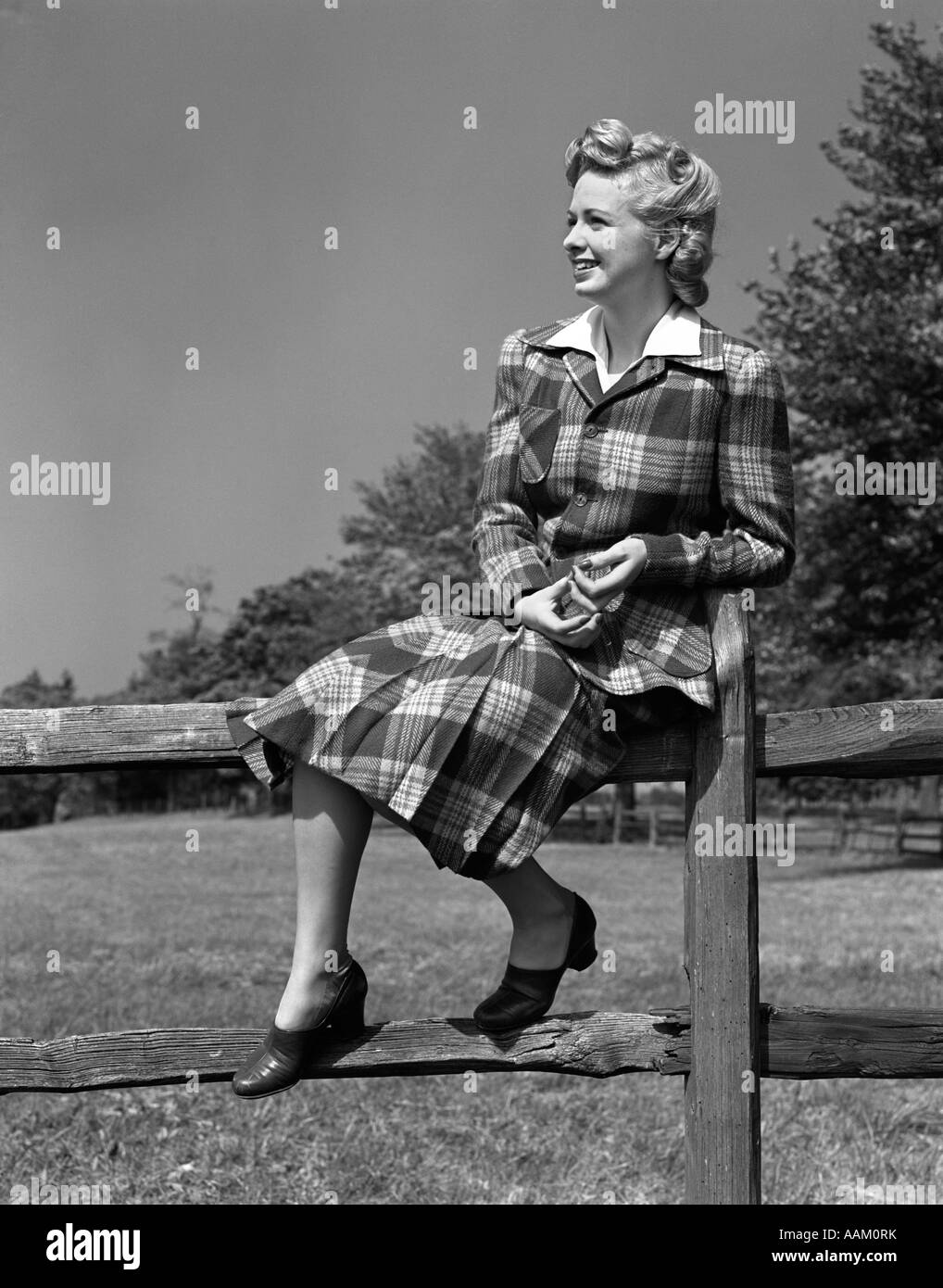 1940s a piena lunghezza Ritratto di donna bionda seduta su una staccionata in legno che indossa tartan scozzese SUIT Foto Stock