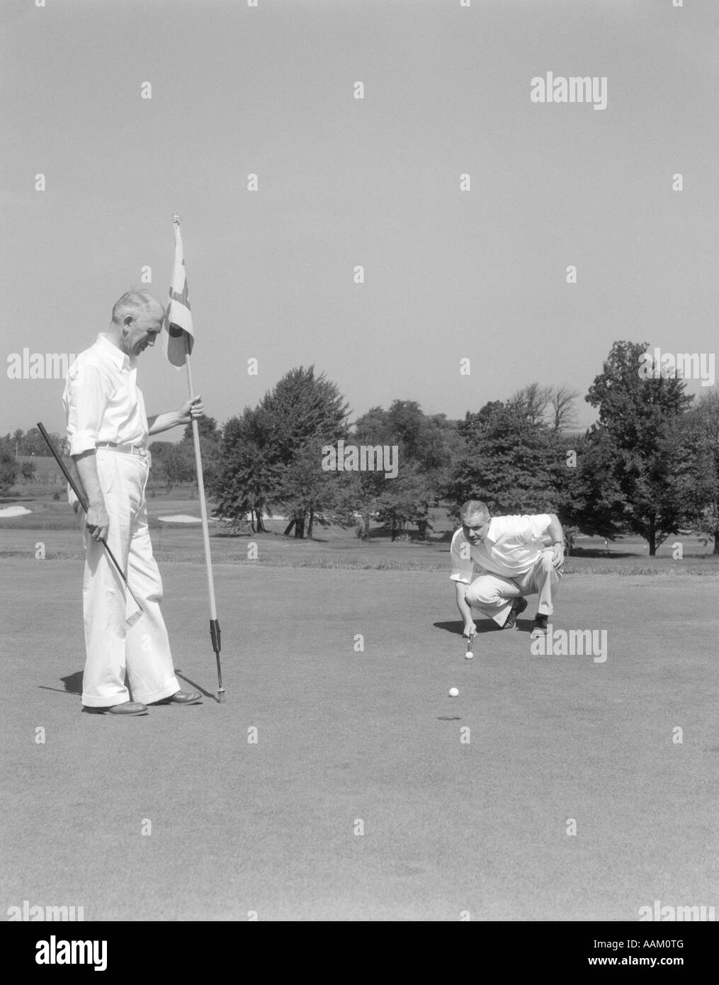 Trenta anni quaranta uomini anziani sul golf verde indicatore di mantenimento di altri si inginocchia allineando il suo PUTT Foto Stock