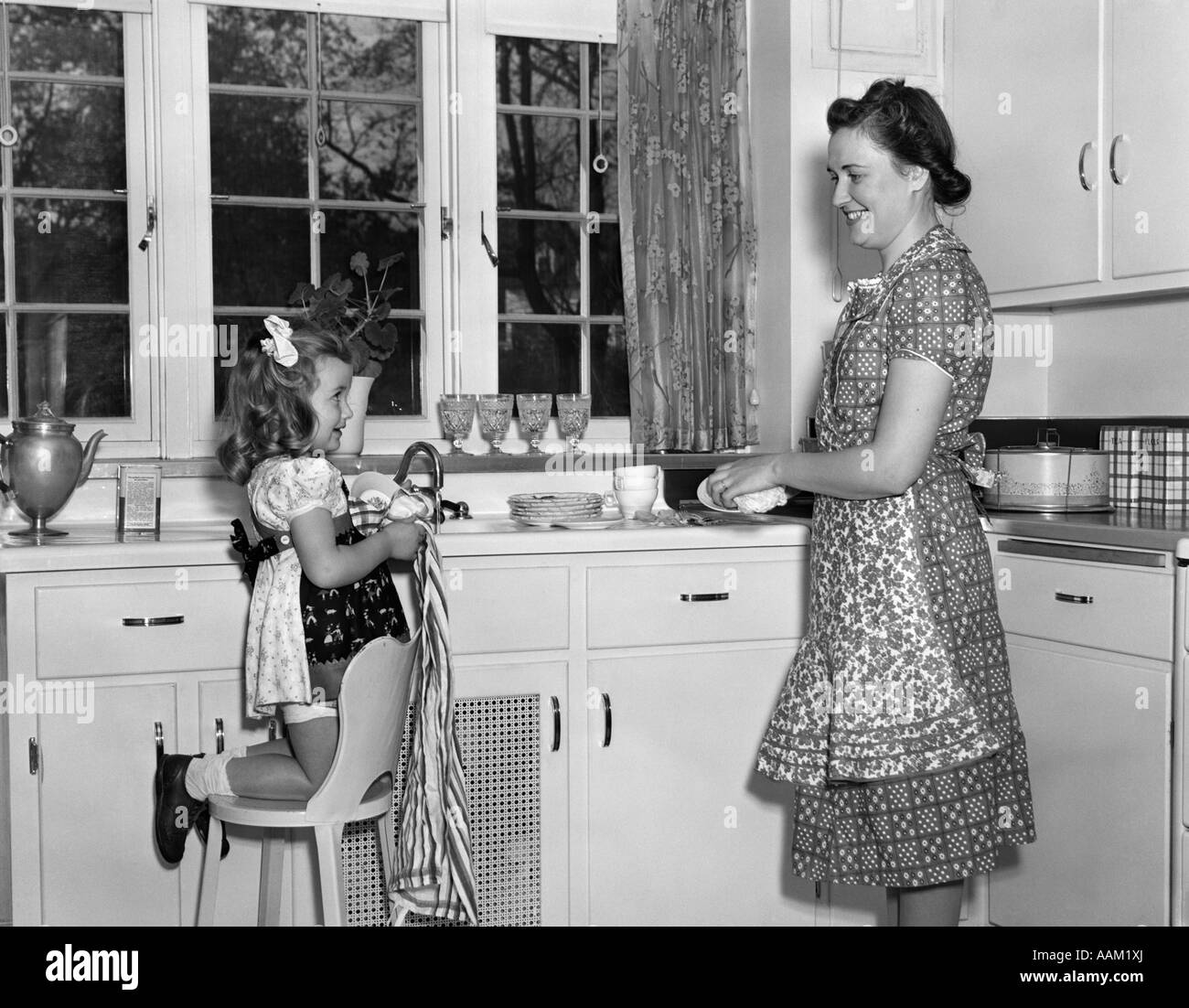 1930s 1940 Madre Donna con bambina figlia inginocchiata su una sedia ad aiutare con le operazioni di lavaggio e di asciugatura stoviglie IN CUCINA Foto Stock