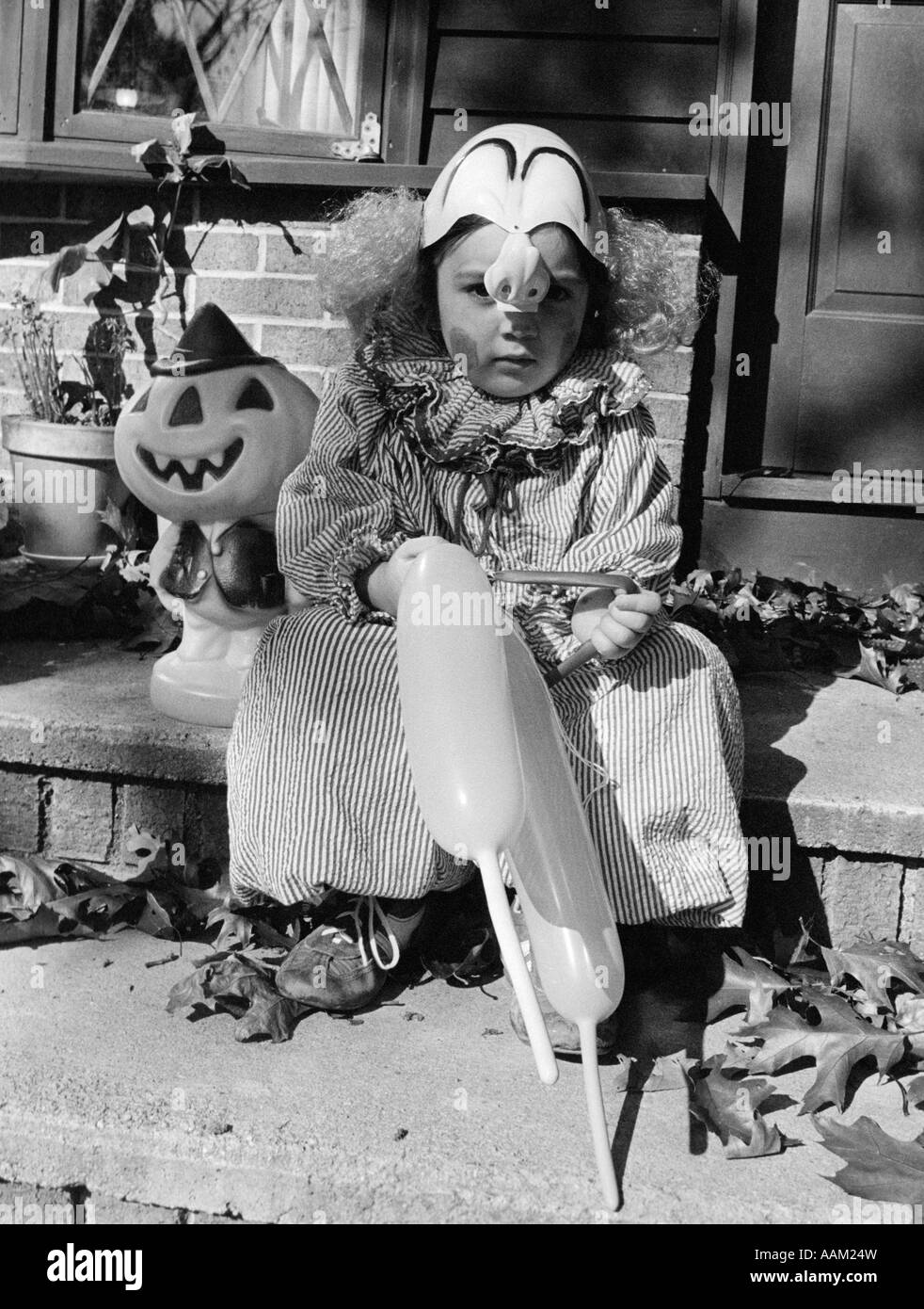 Anni Settanta il bambino nel Dolcetto o scherzetto COSTUME CLOWN SEDUTO SULLA PORTA ANTERIORE FASE palloncini di contenimento Foto Stock