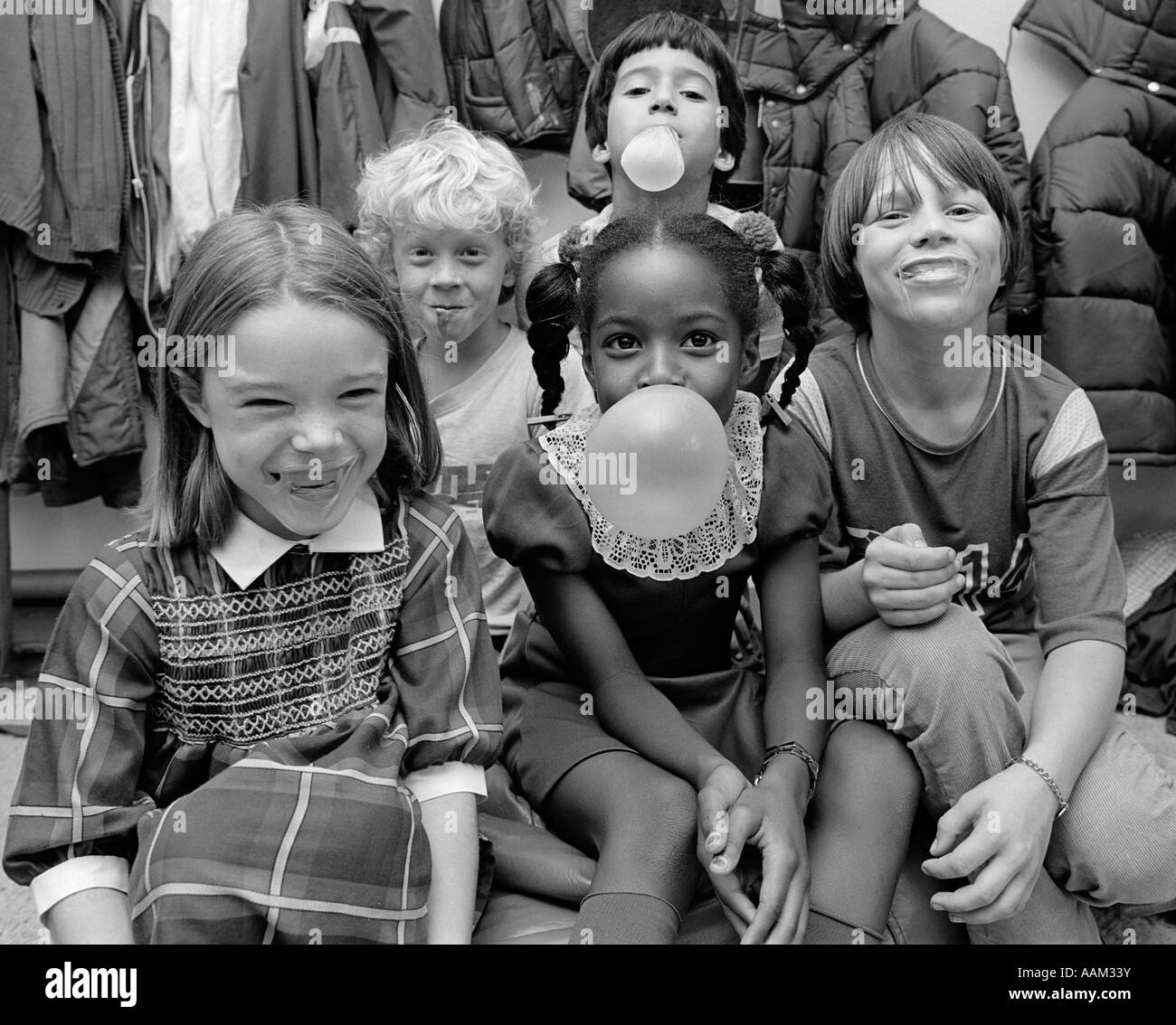 Degli anni Ottanta un gruppo di cinque bambini di gomme da masticare e soffiare bolle ridere indoor Foto Stock