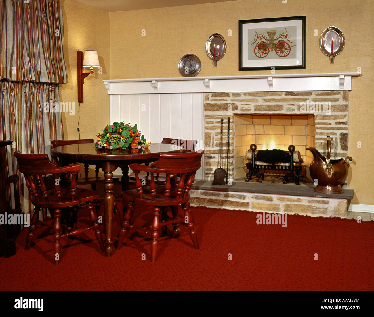 Anni sessanta anni settanta caminetto a legna di pietra paese interiore mobilio coloniale tavolo sedie tappeto rosso appliques mantello Foto Stock