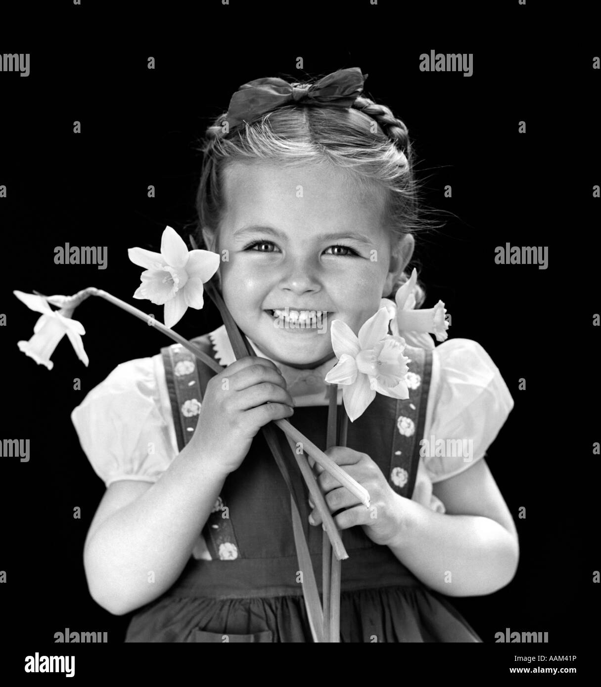 1940s sorridente ragazza mantenendo la molla narcisi che indossa il ponticello con treccia di capelli trattenuto sulla sommità della testa con archetto Foto Stock