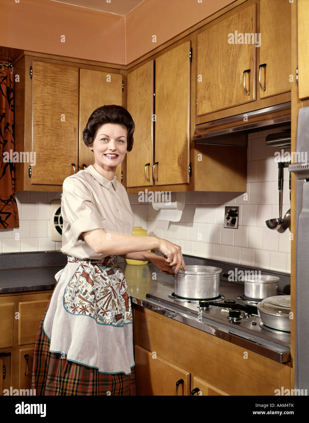Anni sessanta donna sorridente casalinga di indossare un grembiule  agitazione pentola di cottura a fornello da cucina Foto stock - Alamy