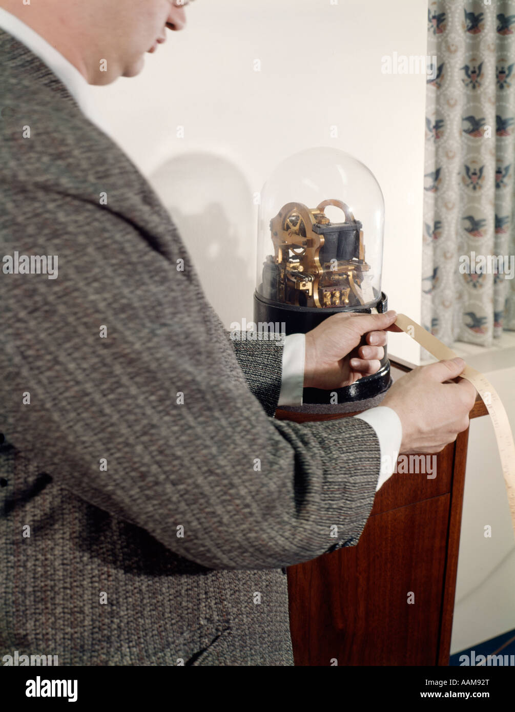 Anni sessanta retrò uomo lettura Ticker tape IN UFFICIO IN PIEDI DA antichi Ticker tape macchina con cupola in vetro Foto Stock