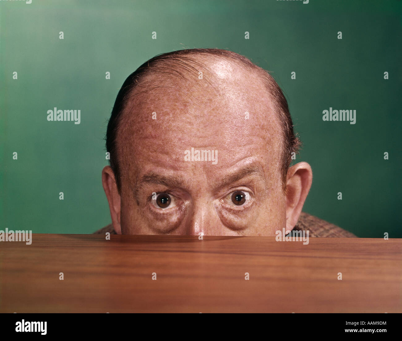 Anni sessanta BALDING MAN PEEKING SU DESKTOP CON solo la metà superiore della testa che mostra Foto Stock Anni sessanta BALDING MAN PEEKING SU DESKTOP CON solo la metà superiore della testa che mostra Foto Stock