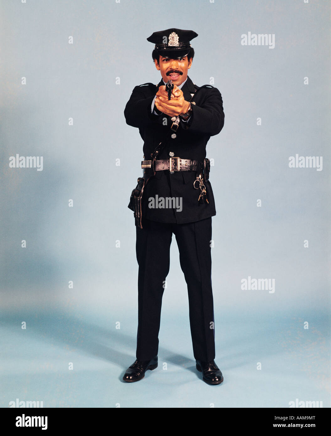 Anni Settanta a figura intera in piedi poliziotto officer uomo pistola di puntamento in telecamera afro-americano STUDIO DI POLIZIA Foto Stock
