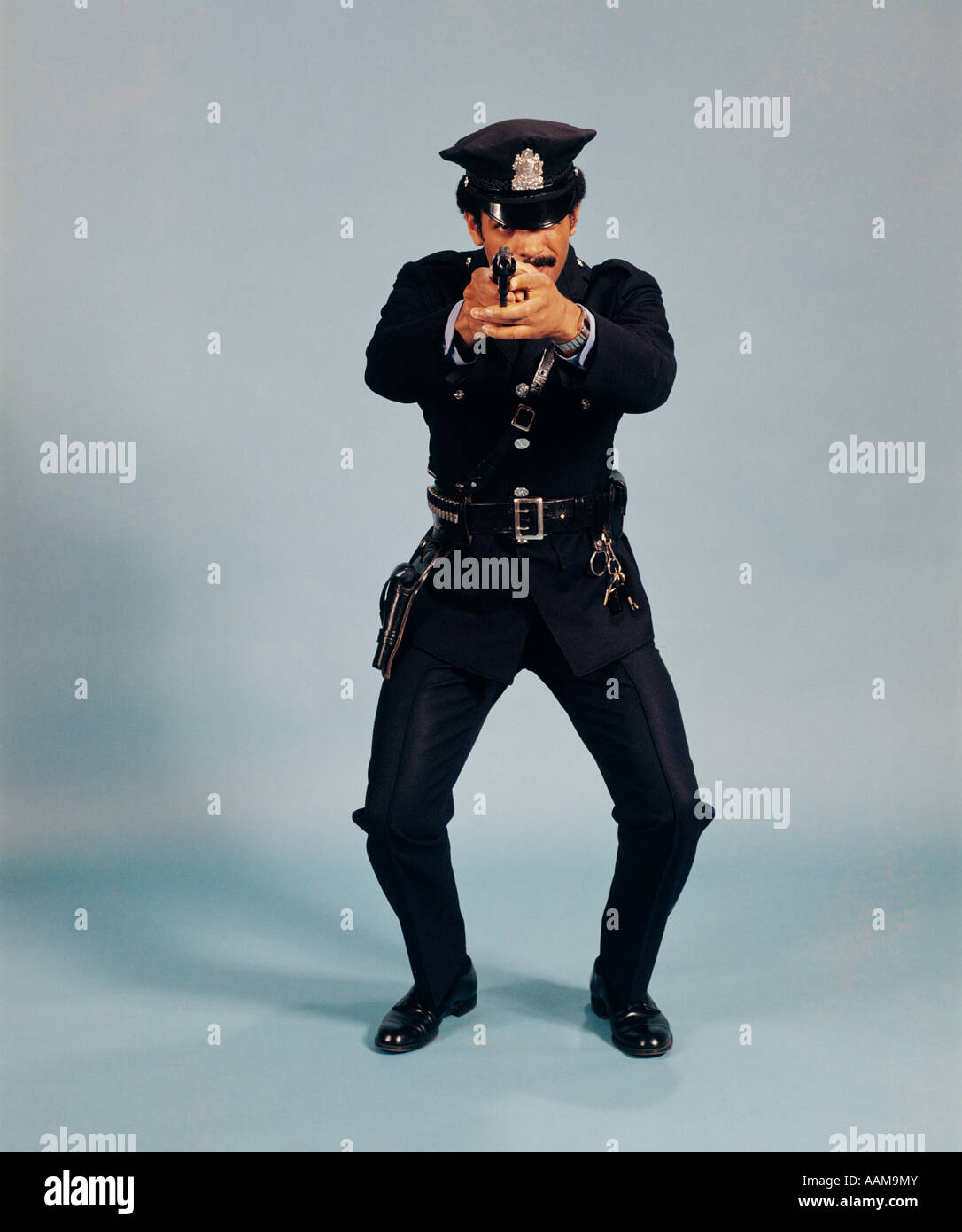 Anni Settanta a piena lunghezza ufficiale di polizia uomo pistola rivolta all azione della videocamera ATTEGGIAMENTO UNIFORME PERMANENTE AFRICAN-AMERICAN Foto Stock