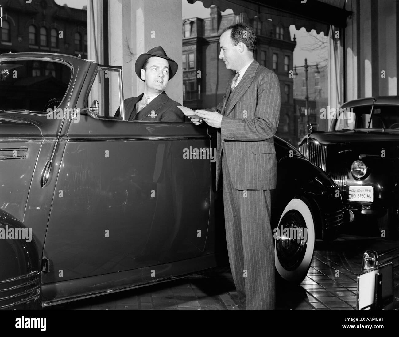 1940s uomo sorridente HAT SEDUTA Cabrio coupe top down parlando venditore PIN STRIPE tuta showroom automobilistico Foto Stock