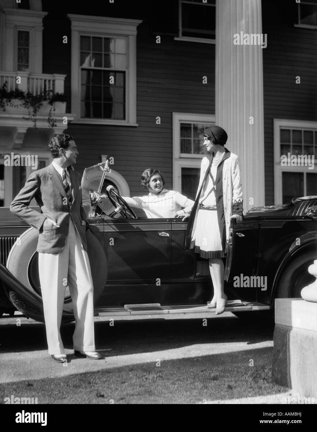 Trenta uomini e due donne in abiti eleganti con TOURING CAR parcheggiata di fronte elegante casa di grandi dimensioni Foto Stock