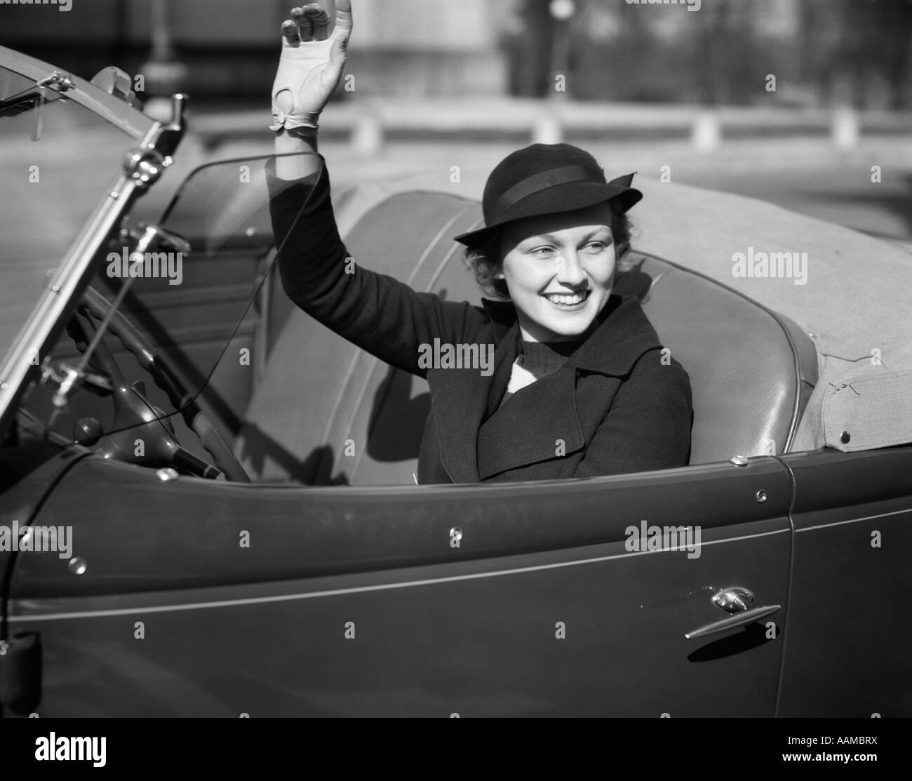 1930s donna sorridente GUIDA ROADSTER CONVERTIBILE AUTOMOBILE agitando la mano guantata Foto Stock