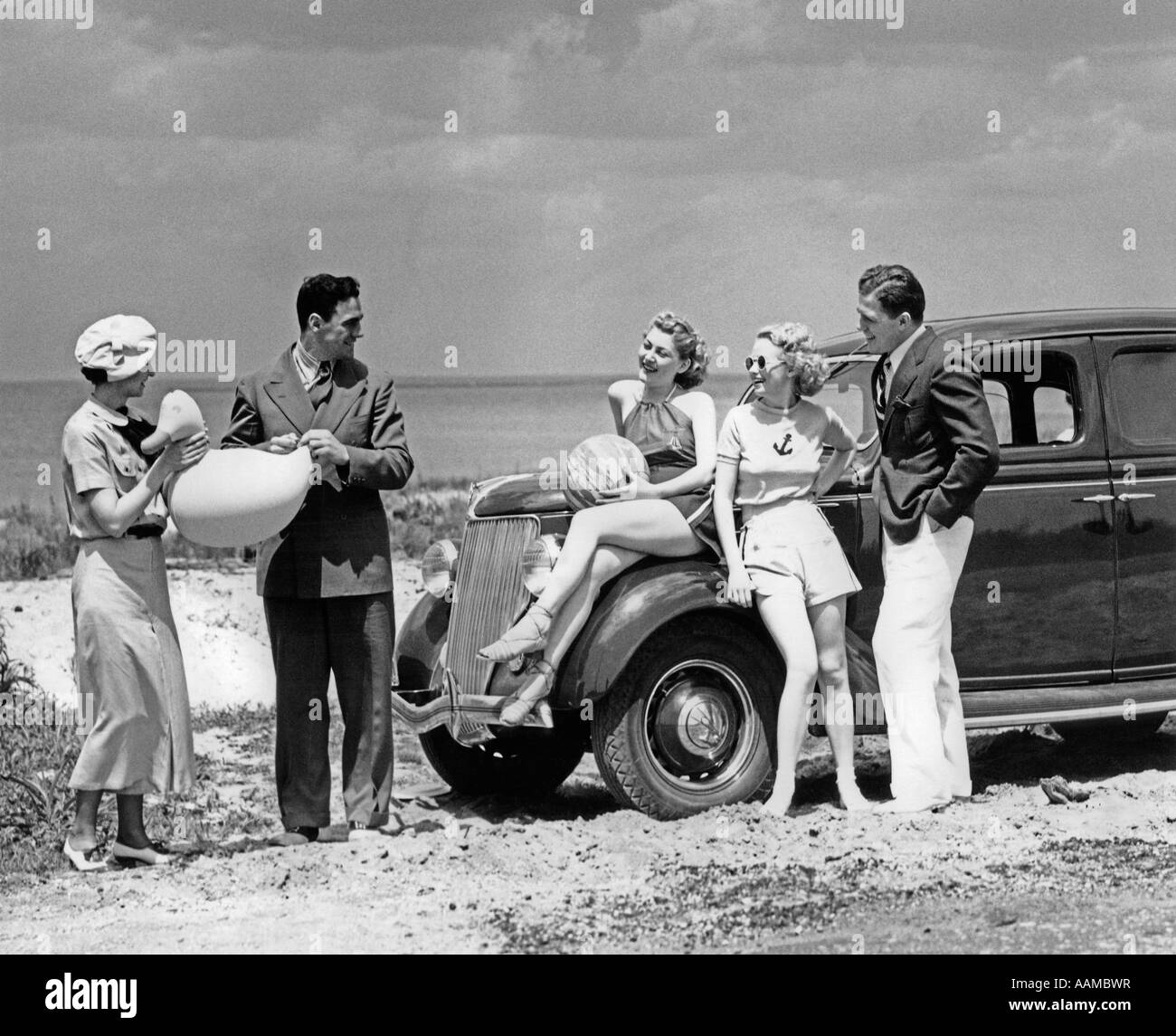 1930 un gruppo di cinque uomini & donne a 1936 Ford V-8 parcheggiato lungo la riva giocando con il gonfiabile di giocattoli da spiaggia Foto Stock