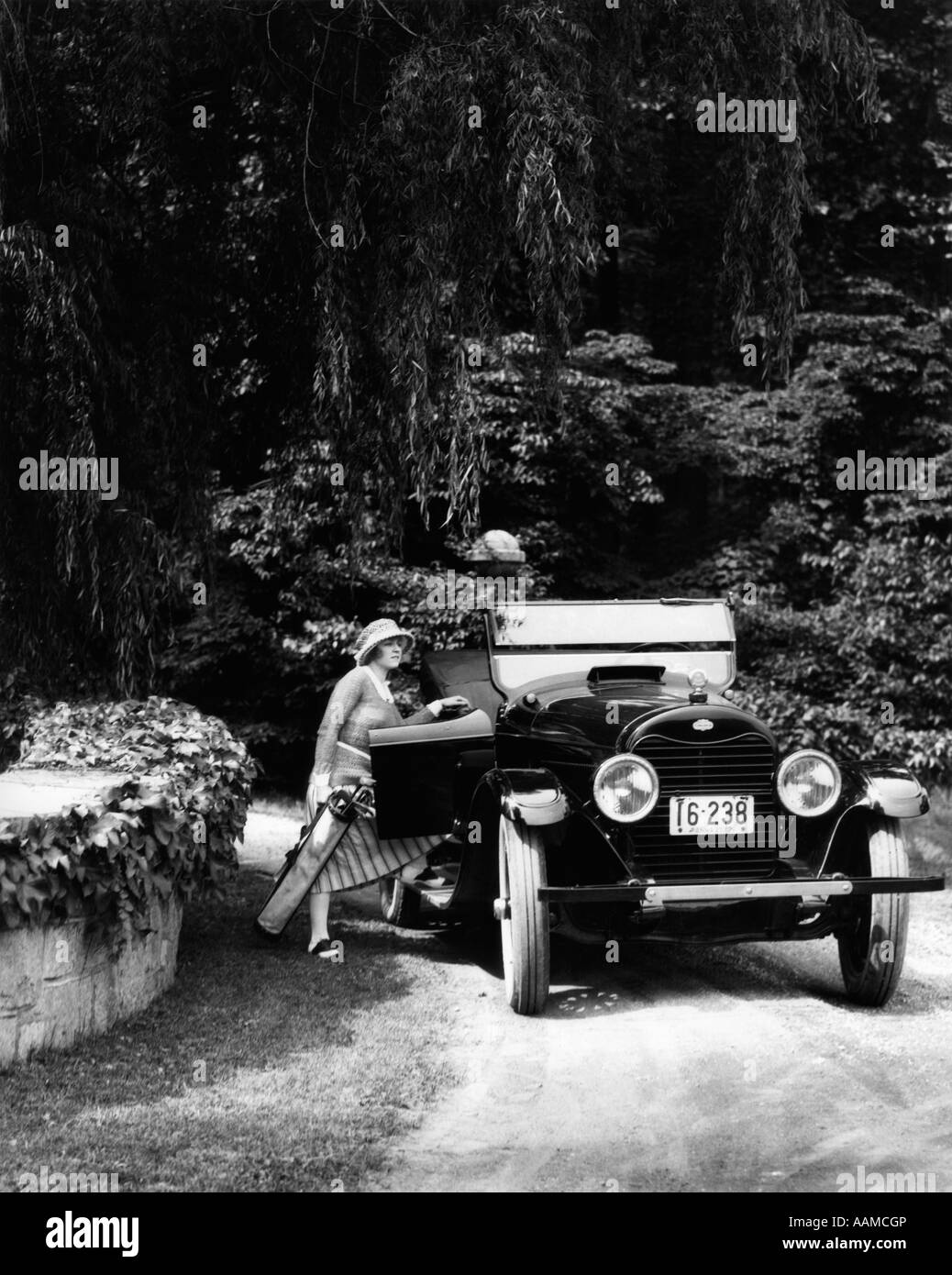 1920s donna di entrare nel lato passeggero della porta auto borsa da golf nella zona boschiva Foto Stock