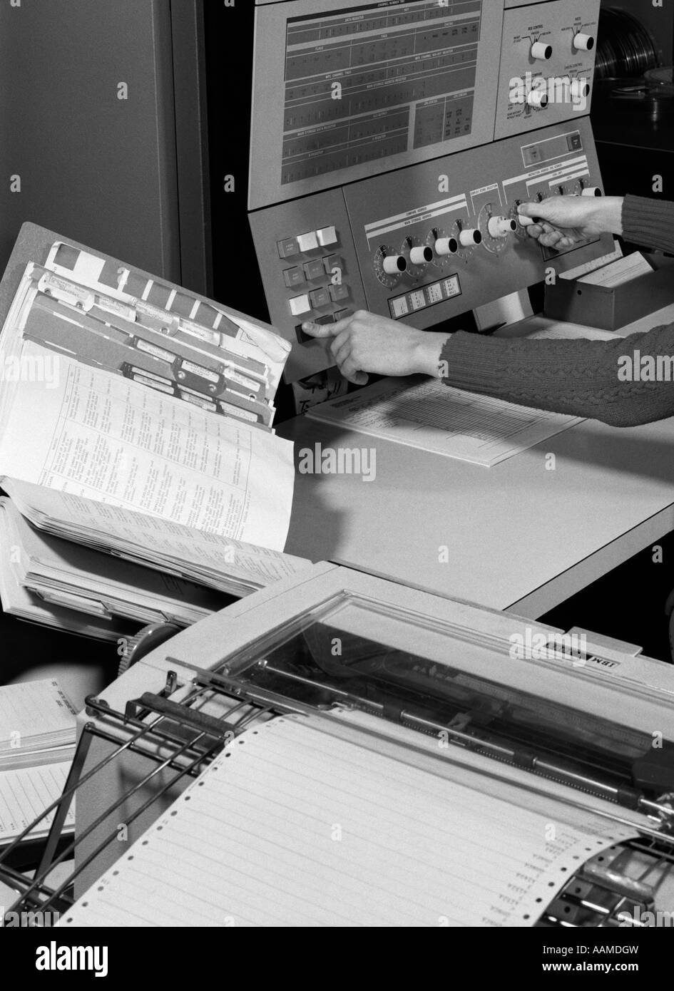 Anni sessanta donna raggiungendo a mano in avanti per regolare le manopole e i pulsanti sul computer di grandi dimensioni con sistema manuale di spessore impostato su lato Foto Stock