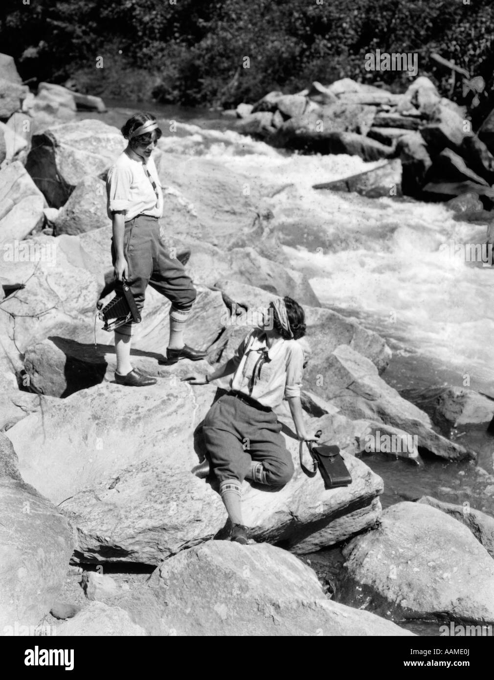 1920s due donne sorelle sulle rocce dal Creek a parlare tenendo la fotocamera di piegatura Foto Stock 1920s due donne sorelle sulle rocce dal Creek a parlare tenendo la fotocamera di piegatura Foto Stock