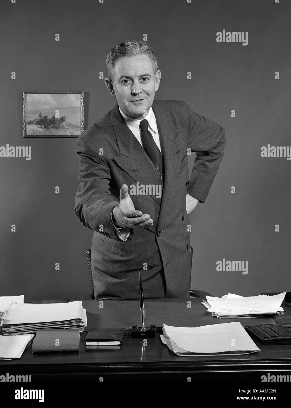 Anni Cinquanta uomo sorridente imprenditore venditore di raggiungere attraverso DESK per agitare le mani Foto Stock