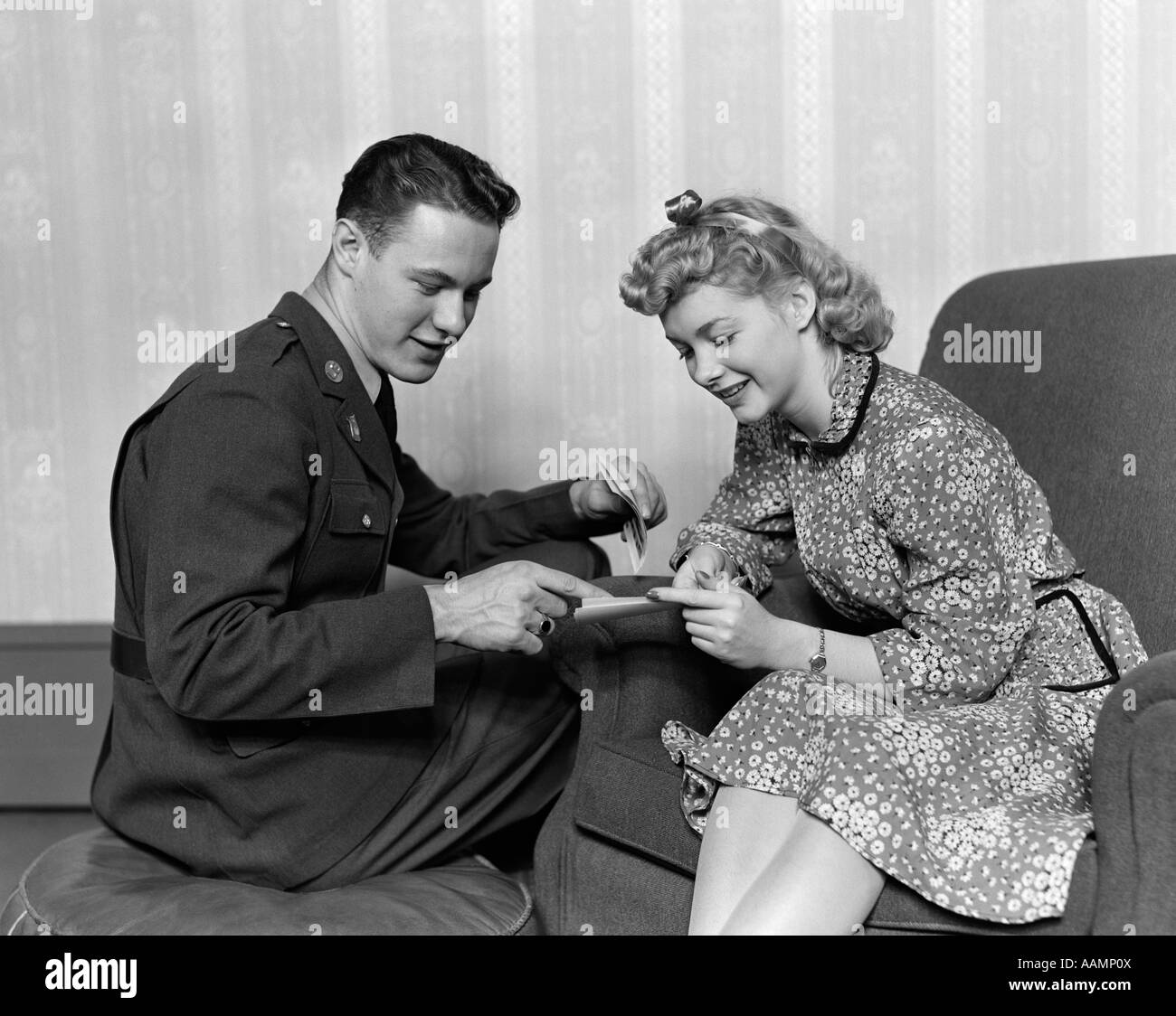 1940s un tempo di guerra romanticismo giovane uomo in uniforme militare donna in abito di stampa seduto in poltrona a sorridere guardando le carte Foto Stock