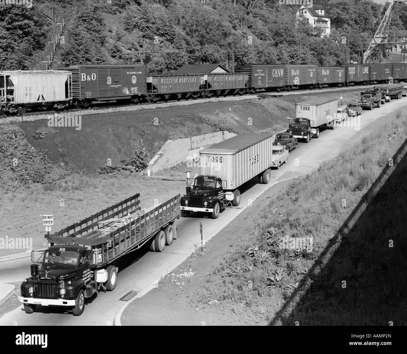 Anni Cinquanta la linea di traffico con molti camion e auto & treno merci passando sulla collina adiacente Foto Stock