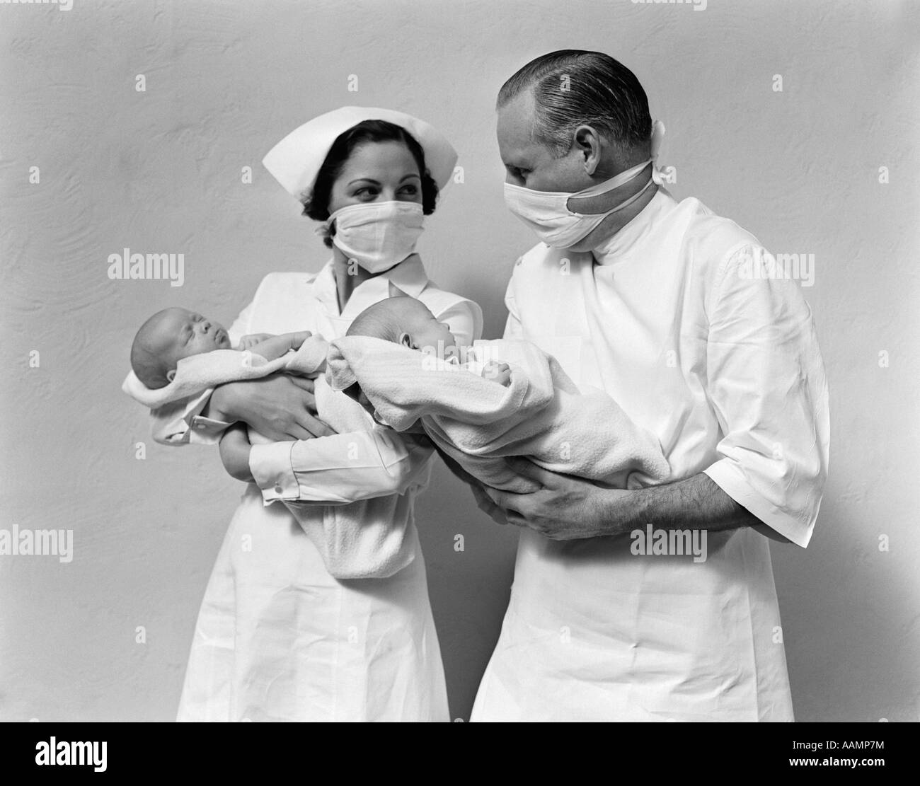 1930s 1940s uomo donna medico infermiere indossando maschere sterile tenendo Neonato Neonati TWIN Foto Stock