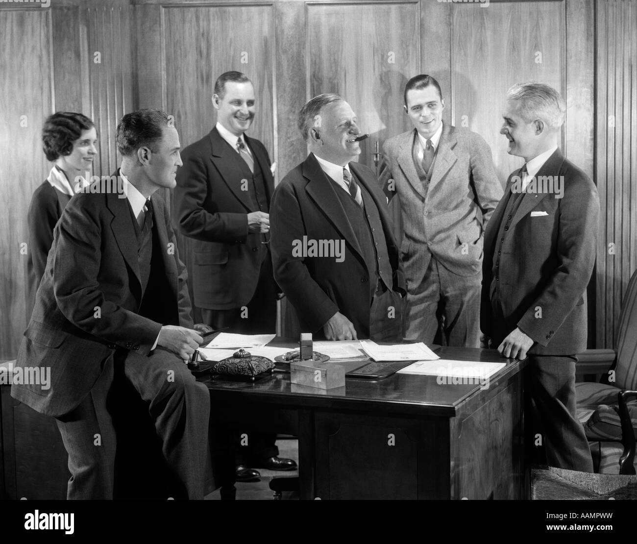 1930 Ufficio sorridente gruppo quattro uomini una donna boss di fumare il sigaro parlando incontro quinto uomo Foto Stock