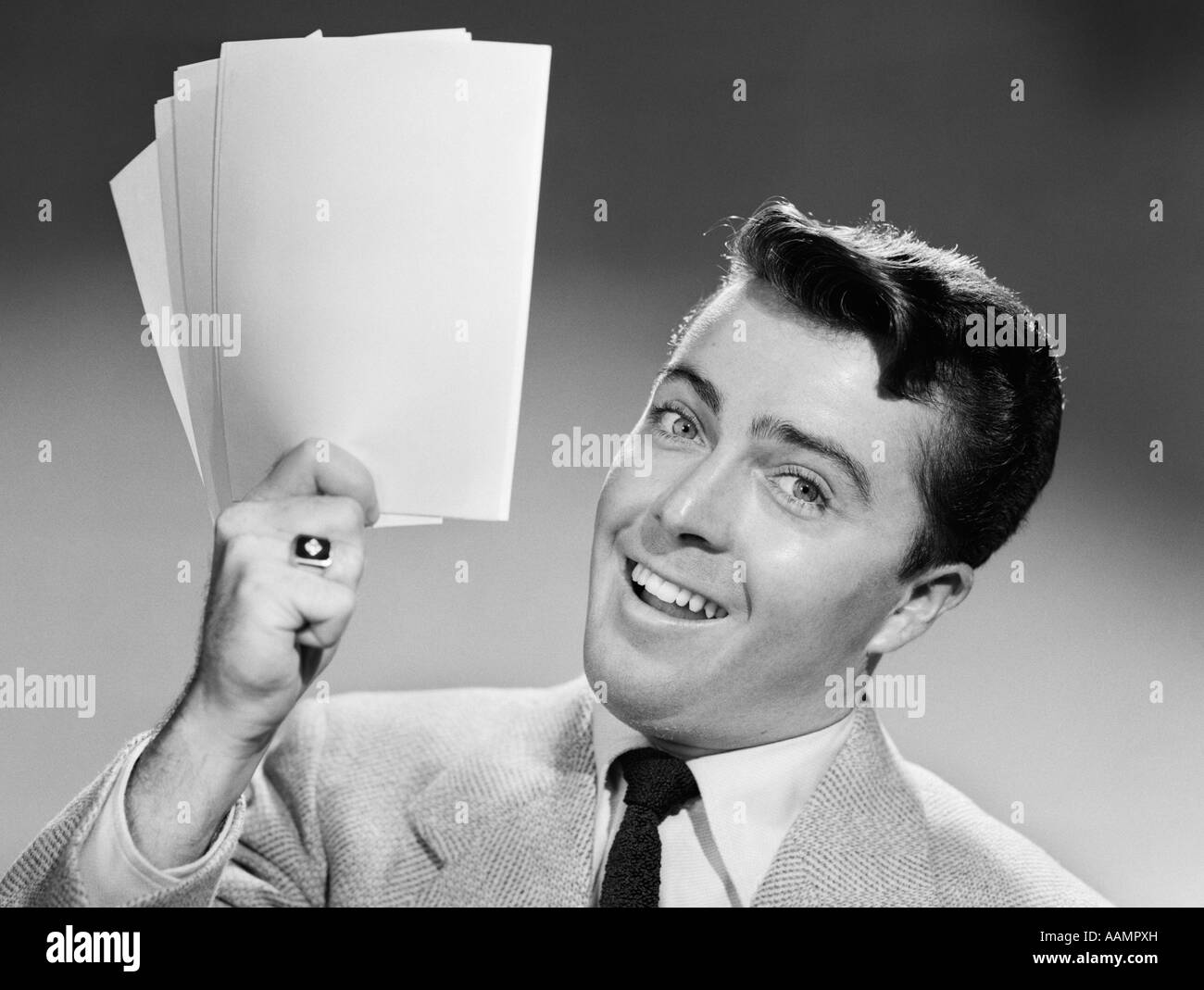 Anni Cinquanta sorridente giovane imprenditore della tuta e cravatta mantenendo la manciata di carte Foto Stock