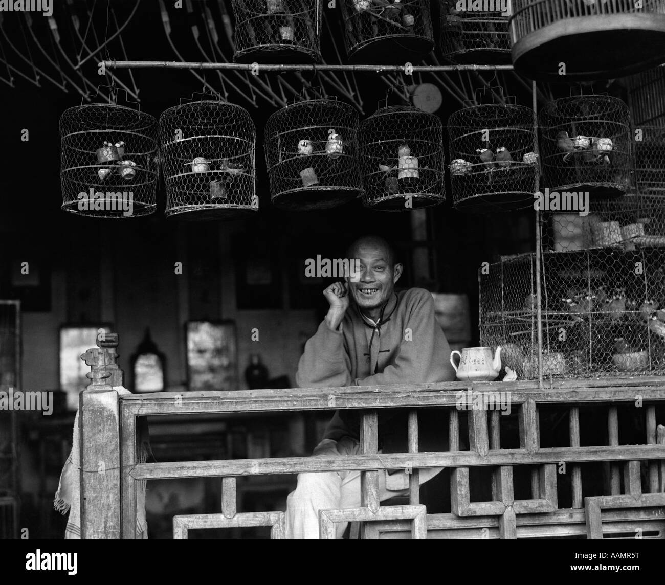 1920s 1930 sorridente uomo cinese BIRD VENDER VENDITORE IN NEGOZIO CON VOLIÈRES NELLA CITTÀ DI SHANGHAI IN CINA Foto Stock