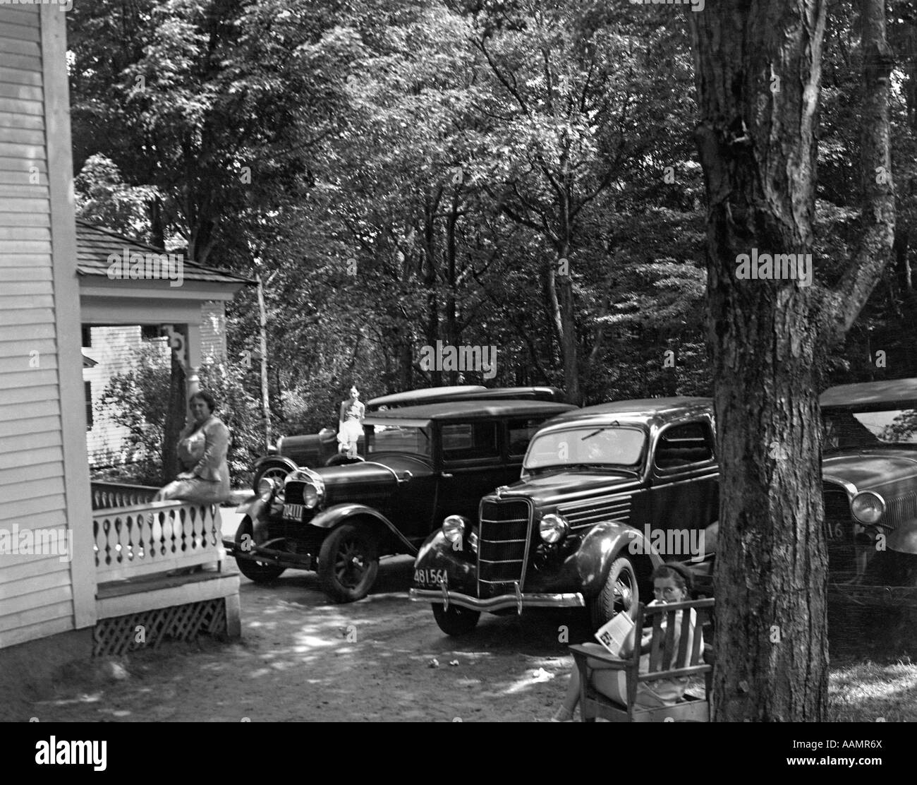 Trenta vetture parcheggiate nel cortile anteriore DONNA SUL BANCO DI PORTICO LAZY SUMMER RESORT COTTAGE di cabina del New Hampshire USA Foto Stock