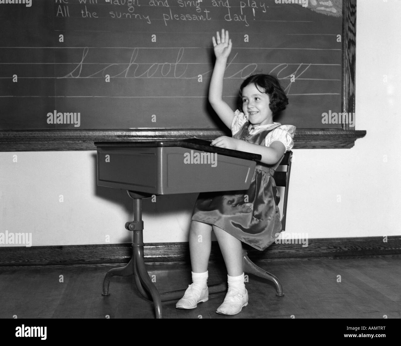 1930s 1940s sorridente ragazza seduta alla scrivania alzando la mano Foto Stock