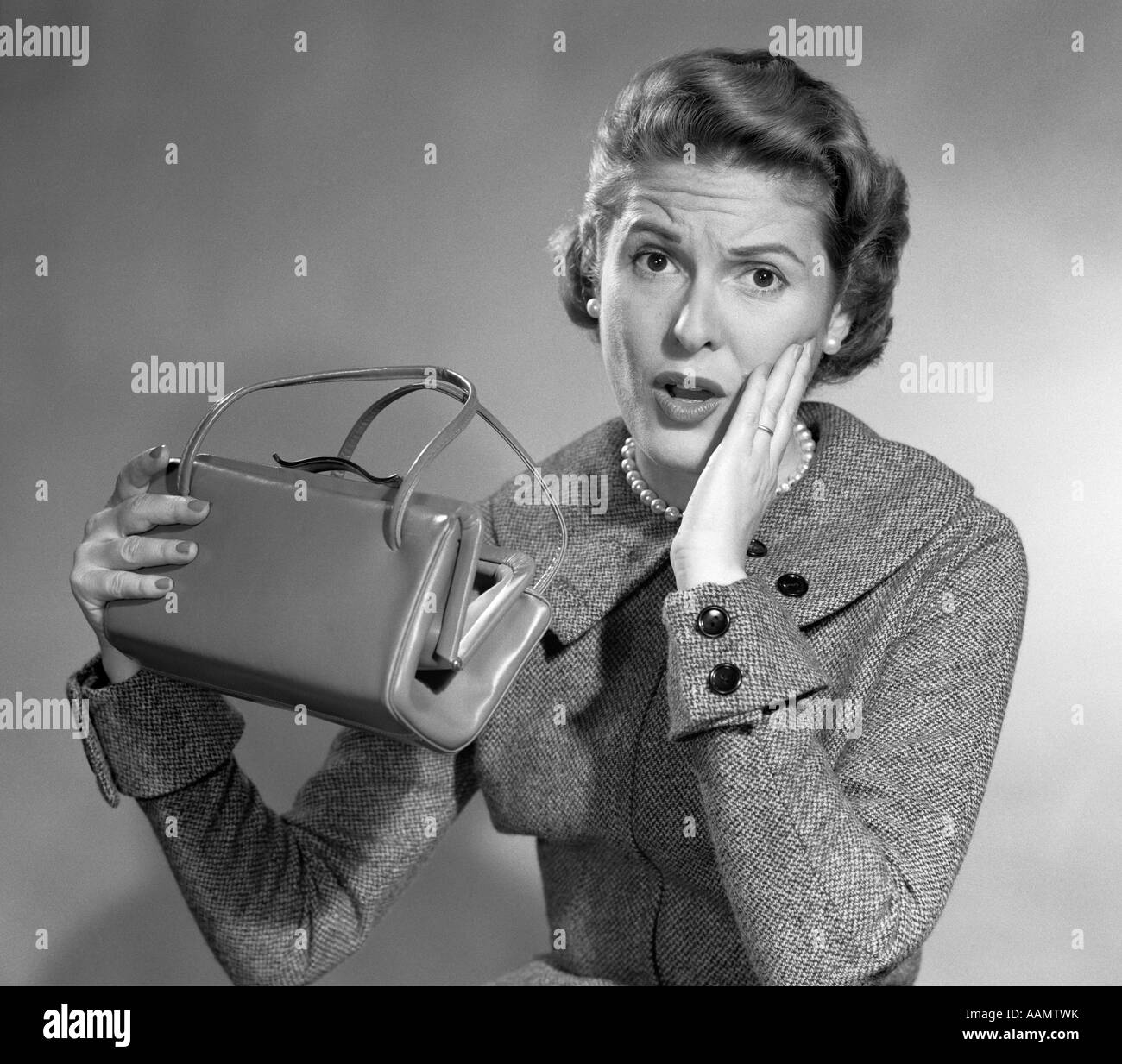 Degli anni Cinquanta ha rotto la donna sorpresa l'espressione del viso mano a guancia HOLDING vuoto borsetta guardando la fotocamera Foto Stock