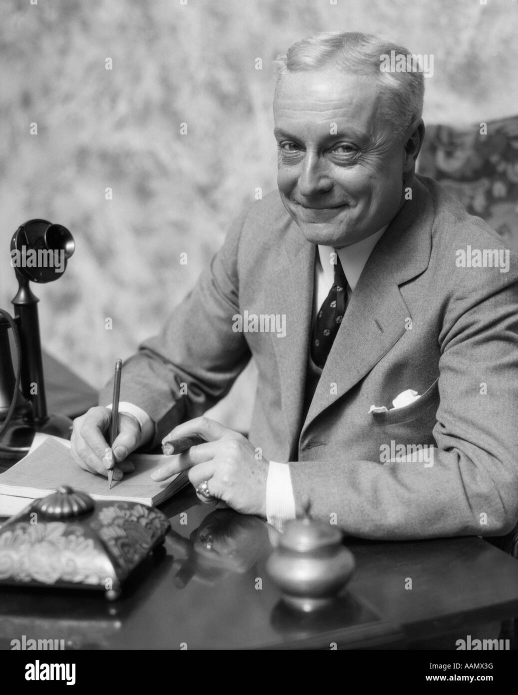 1920s 1930 uomo sorridente imprenditore venditore seduto alla scrivania di fumare il sigaro scrivere un memo Foto Stock