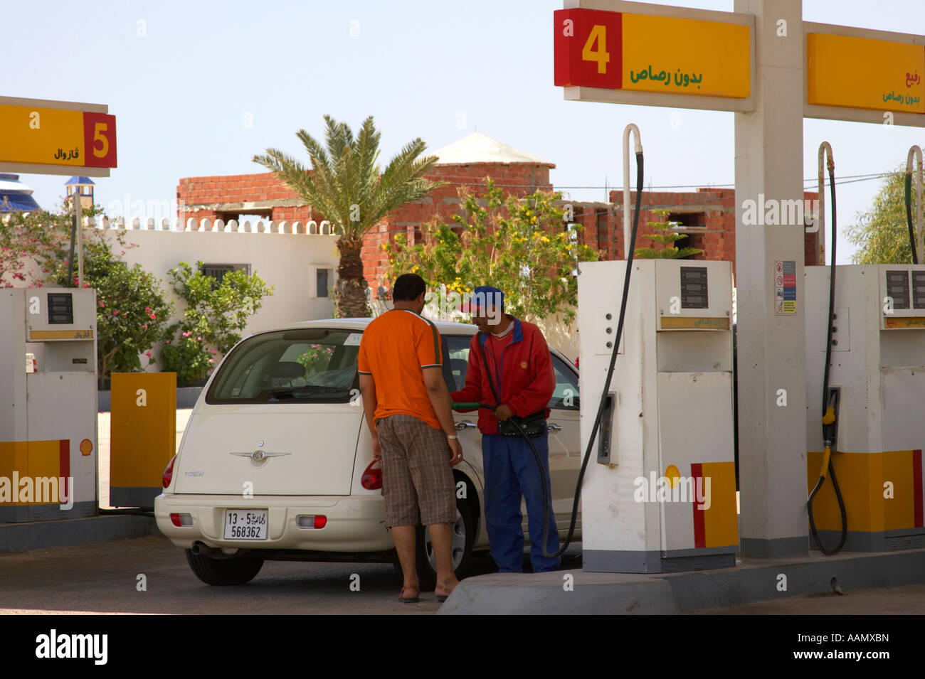 Stazione di benzina lavoratore locale di riempimento Chrysler PT Cruiser auto con benzina senza piombo guardato da driver nel piazzale della stazione shell Foto Stock