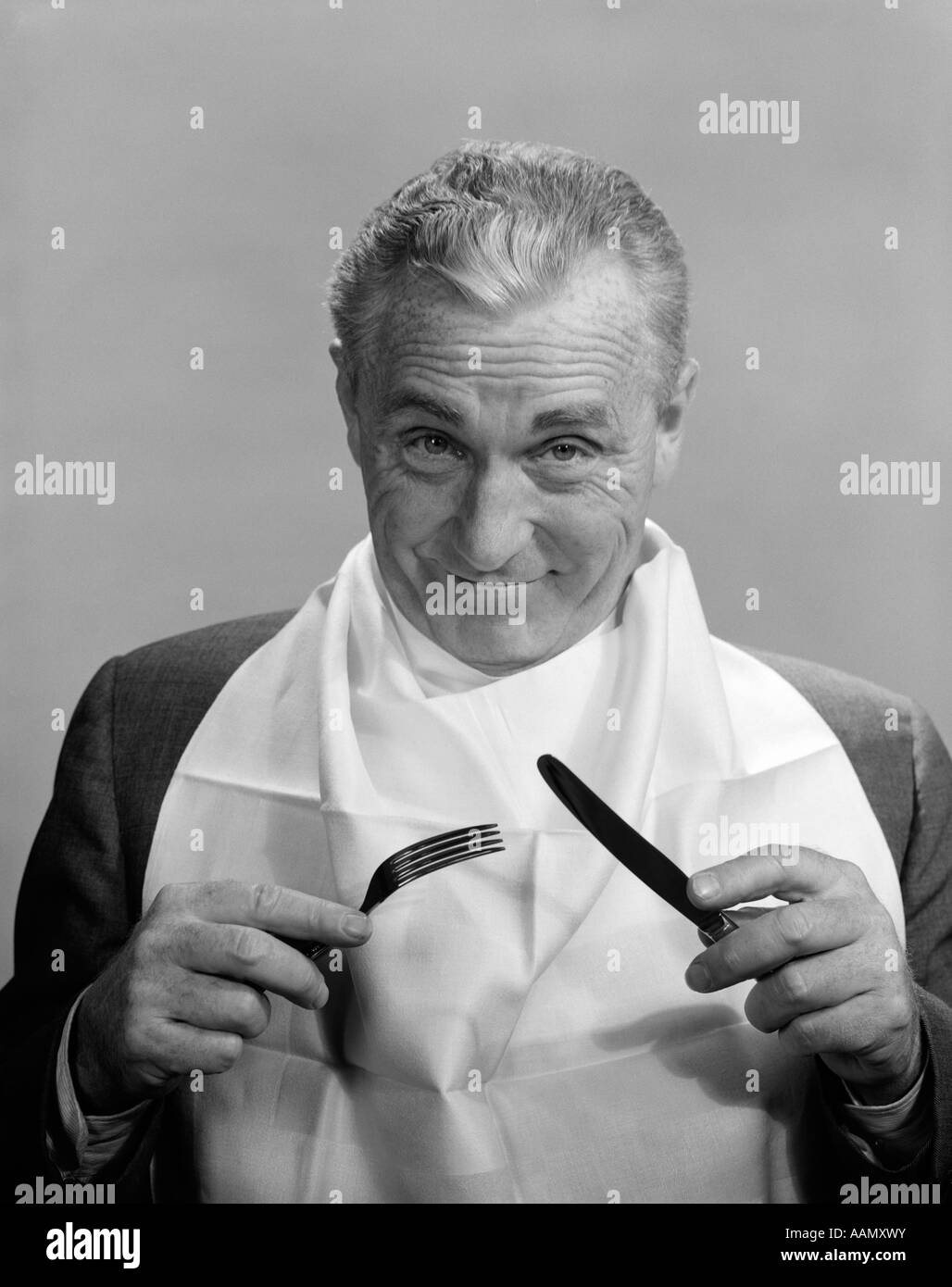 Anni Cinquanta anni sessanta uomo anziano usura igienico come la BIB sorridente tenendo il coltello e forchetta mangiare mangiare anticipazione dieta ALIMENTARE NUTRIZIONE Foto Stock