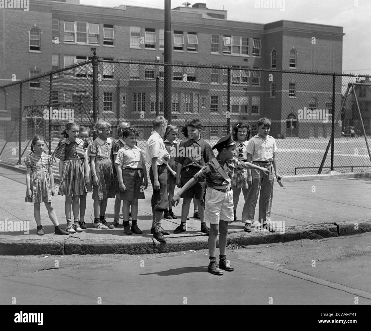 1930s PATERSON NJ BOY CROSSING GUARD HOLDING gruppo posteriore del gli studenti della scuola elementare in attesa al cordolo di Cross Street Foto Stock