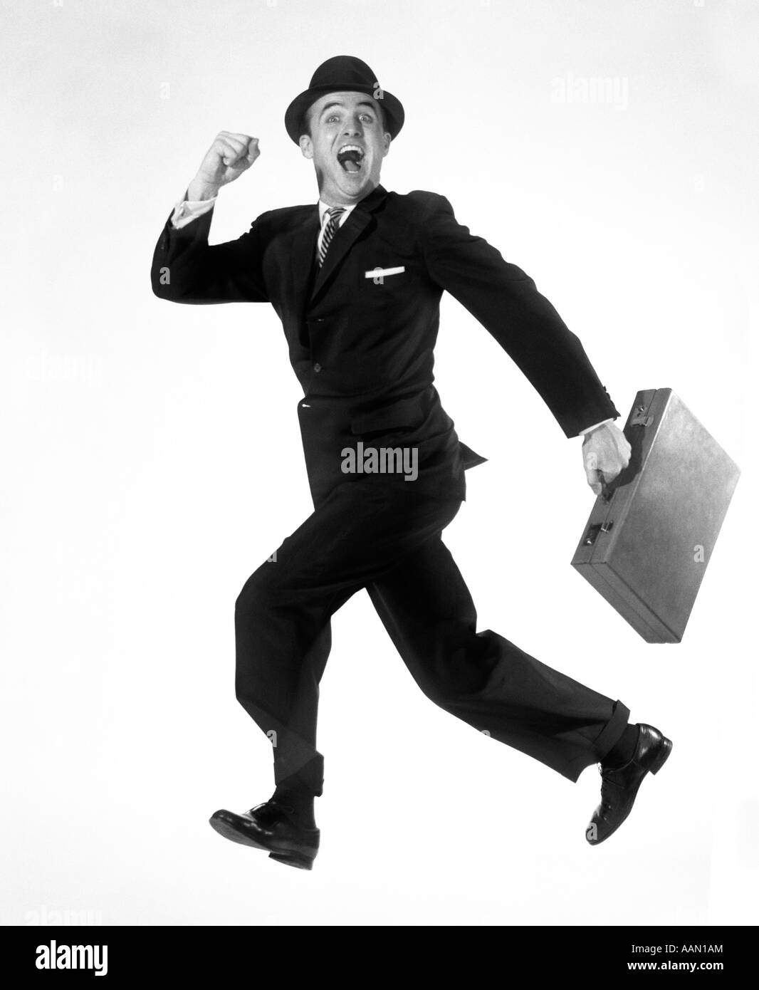 Anni Cinquanta anni sessanta felice eccitato esuberante uomo salti in aria in funzione portante valigetta ventiquattrore indossando BUSINESS SUIT HAT Foto Stock