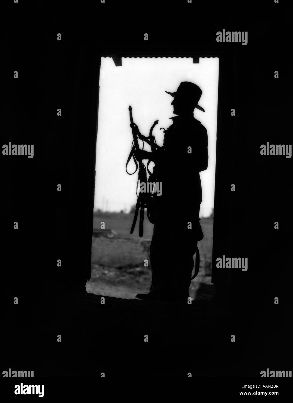 1930s silhouette di un vecchio contadino nel cappello di paglia nel fienile porta cavo di contenimento Foto Stock