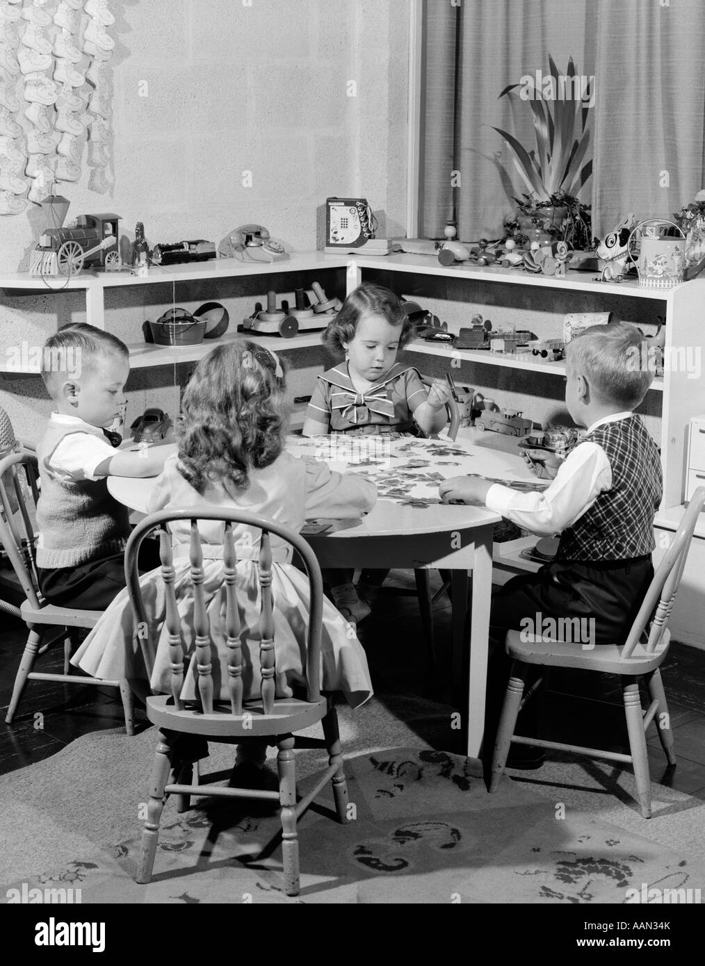 Anni Cinquanta 4 bambini in età prescolare seduto al tavolino rotondo mettendo insieme PUZZLE Foto Stock