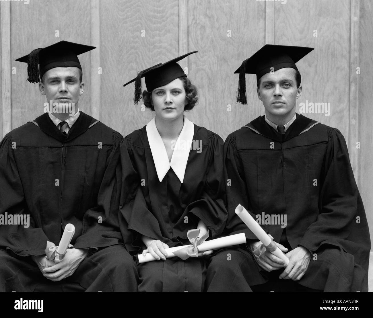 Trenta anni quaranta studenti universitari che indossano vesti di graduazione 2 uomini 1 DONNA HOLDING DIPLOMI guardando la fotocamera Foto Stock